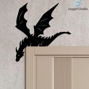 May include: Black dragon wall decor with outstretched wings, perched on a door frame. The dragon silhouette is a detailed cutout, adding a touch of fantasy to any room. The dragon's wings are spread, and the tail is extended.