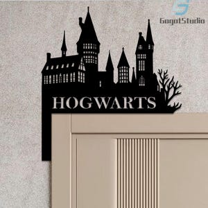 May include: Black metal wall art featuring the silhouette of Hogwarts castle with the word "HOGWARTS" in white lettering. The castle design includes towers, windows, and a tree. The art is mounted on a light-colored door.