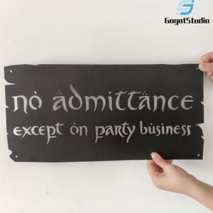 May include: A black rectangular sign with the words "no admittance except on party business" in silver lettering. The sign has a rustic, distressed edge design and is held up by two hands.