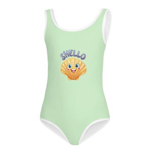 Puede incluir: Un bañador de una pieza de color verde claro con ribete blanco. El bañador presenta una ilustración de dibujos animados de una concha sonriente con el texto "Shello" encima.