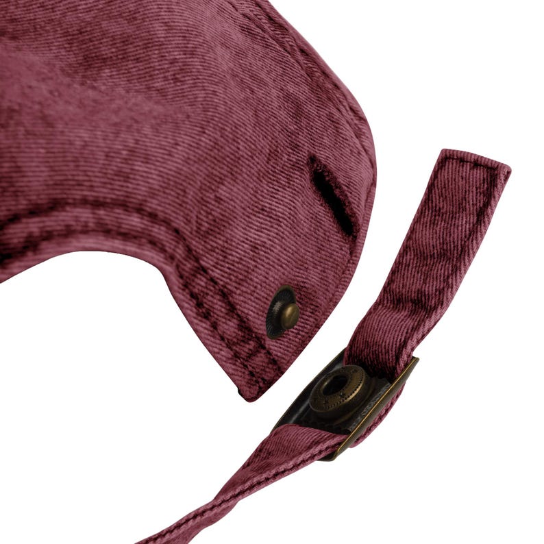 May include: Close-up of a maroon baseball cap with a curved peak and adjustable strap. The cap features a metal clasp and a button detail. The fabric has a textured appearance.