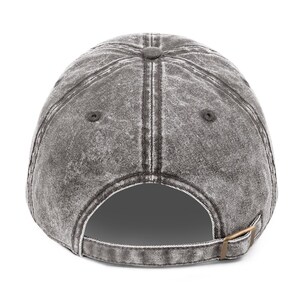May include: A grey, distressed baseball cap with a curved peak. The back of the cap has an adjustable strap with a metal buckle. The cap has a worn, vintage appearance.