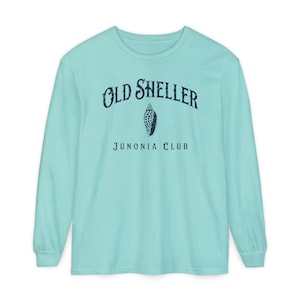 May include: A light turquoise long-sleeve shirt with the text "OLD SHELLER" arched across the top, a seashell graphic in the center, and "JUNONIA CLUB" below. The text and graphic are in a distressed navy blue font.