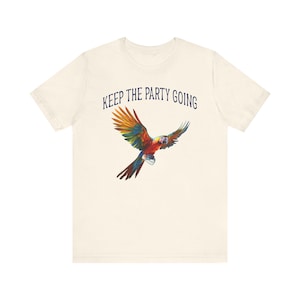 May include: Cream-colored t-shirt featuring a colorful parrot graphic with outstretched wings. The text "KEEP THE PARTY GOING" is printed above the bird in navy blue. The parrot has red, yellow, green, and blue feathers.