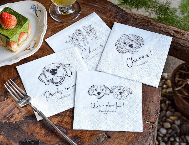 May include: White square napkins with black line drawings of dogs and text. One napkin says "Cheers! Love, Sadie", another says "Drinks on me Love, Parker", and another says "We do too! Diana & Christian 10/07/23".
