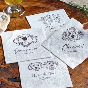 May include: White paper napkins with dog illustrations and text. One napkin says "Drinks on me! Love, Parker", another says "Cheers! Love, Sadie", and a third says "We do too! Diana & Christian 10/02/25".