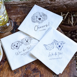 May include: White paper napkins with black line drawings of dogs and a cat. One napkin says "Cheers! Love, Sadie." Another says "We do too! Diana & Christian 10/07/25." The third says "We do too! Love Parker and Benji."