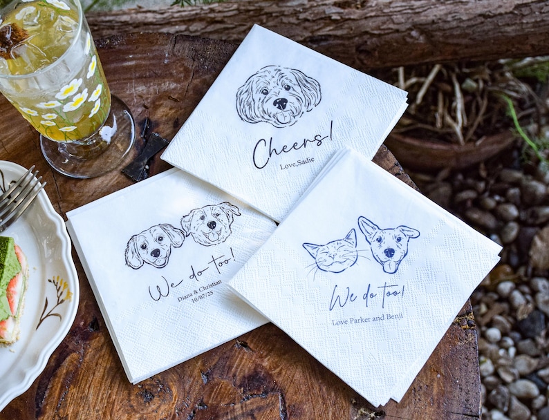 May include: White paper napkins with black line drawings of dogs and a cat. One napkin says "Cheers! Love, Sadie." Another says "We do too! Diana & Christian 10/07/25." The third says "We do too! Love Parker and Benji."