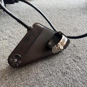 May include: A dark brown, triangular-shaped component with a circular, fan-like detail on one end. A metal clamp secures a black tube to the component. Black cables extend from the device, suggesting it is part of a larger system.