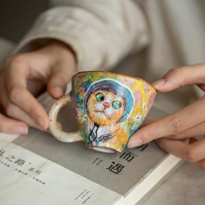 Peut inclure: Tasse en céramique colorée avec une illustration fantaisiste d'un chat astronaute. La tasse est ornée de motifs floraux et abstraits dans des tons de jaune, orange, bleu et vert. Elle possède une petite anse.