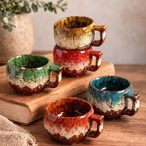 Peut inclure: Ensemble de tasses à café en céramique de différentes couleurs, dont vert, bleu, rouge et marron. Chaque tasse a un glaçage unique et une petite anse. Les tasses sont empilées et disposées sur une surface en bois.