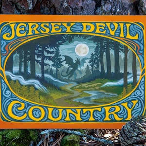 May include: An orange and blue art print with the words "Jersey Devil Country" in a decorative font. The artwork depicts a forest scene with a dragon, a full moon, and a winding river.