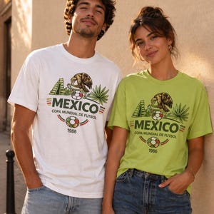Peut inclure: Deux personnes portant des t-shirts blancs et vert citron avec un motif du Mexique. Le motif comprend un aigle, un ballon de football et le texte "MEXICO COPA MUNDIAL DE FUTBOL 1986". Ils portent des jeans bleus.