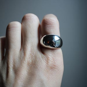 May include: A silver ring with a large, smooth, rounded dome shape.