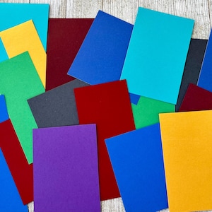 May include: A collection of colorful paper squares in various shades of blue, green, red, yellow, and purple. The squares are arranged in a random pattern on a wooden surface.