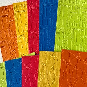 May include: Assortment of colorful cardstock paper with embossed patterns. The patterns include words like "happy birthday" and "birthday" and a pattern of balloons.