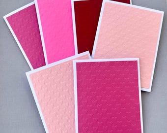 May include: Set of six blank greeting cards with embossed heart patterns in various shades of pink and red. The cards are perfect for sending a heartfelt message.