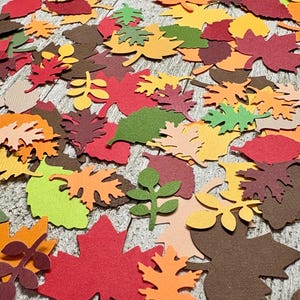 May include: Assortment of fall-themed paper leaves in various shades of red, orange, yellow, and green. The leaves are cut out of paper and have a slightly textured finish.