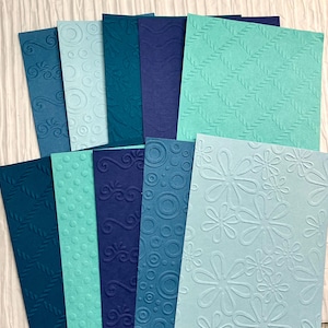 May include: Assortment of 10 textured cardstock sheets in shades of blue and teal. The sheets feature embossed patterns including swirls, dots, and flowers.