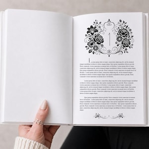 Könnte beinhalten: Ein aufgeschlagenes Buch mit weißen Seiten, schwarzem Textdruck und einer dekorativen Blumenillustration, die die Zahl Eins am oberen Rand der rechten Seite umrahmt. Das Layout enthält einen großen Anfangsbuchstaben L und eine kleine florale Trennlinie.