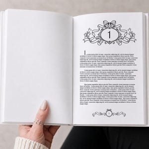 Könnte beinhalten: Ein offenes Buch mit weißen Seiten. Die rechte Seite zeigt ein dekoratives schwarz-weißes Design mit der Zahl 1 in einem ovalen Rahmen. Text ist auf der rechten Seite sichtbar, eine Hand hält das Buch.