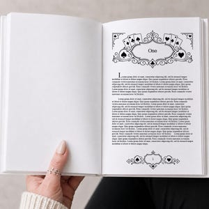 Pode incluir: Um livro aberto com uma página com a palavra "One" dentro de uma moldura decorativa com símbolos de cartas de baralho. A página tem uma borda decorativa com símbolos de cartas de baralho e uma letra inicial grande.