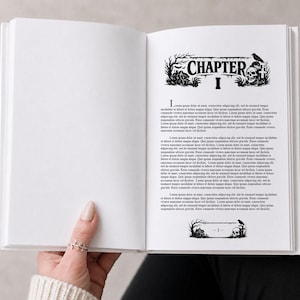 Könnte beinhalten: Offenes Buch mit dem Text "CHAPTER I" über dem Textkörper. Die Kapitelüberschrift zeigt eine gruselige Illustration eines Spukhauses, eines Schädels und eines Raben. Das Buch wird von einer Person offen gehalten.