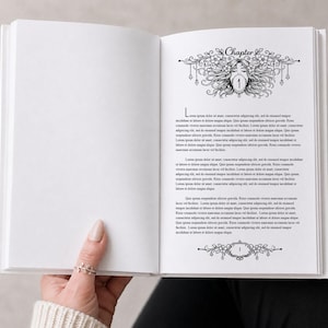 Könnte beinhalten: Offenes Buch mit Text und dekorativen Illustrationen. Die rechte Seite zeigt ein Blumendesign mit einem Gesicht und dem Wort "Kapitel". Die linke Seite ist leer. Eine Hand mit einem Ring hält das Buch.