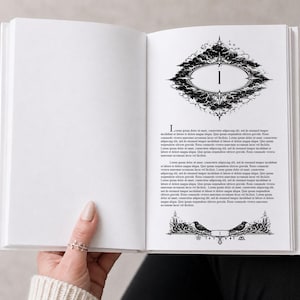 Könnte beinhalten: Ein offenes Buch mit weißem Einband, das eine detaillierte Schwarz-Weiß-Illustration auf der rechten Seite zeigt. Die Illustration zeigt einen dekorativen Rahmen mit der Zahl "1" im Inneren, umgeben von kunstvollen wolkenartigen Designs und Text.
