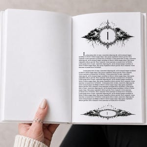 Könnte beinhalten: Ein offenes Buch mit weißen Seiten, gehalten von einer Person. Die rechte Seite zeigt dekorative schwarz-weiße Illustrationen mit der Zahl "1" in verzierten Rahmen. Text füllt die Seite unter den Illustrationen.