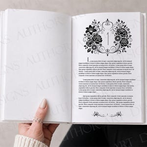 May include: An open book with white pages featuring black printed text and a decorative floral illustration at the top of the right page. The number 1 is centered within the floral design, and a small floral ornament appears at the bottom.