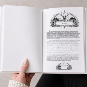 Könnte beinhalten: Ein offenes Buch mit weißem Einband, gehalten von einer Hand. Die rechte Seite zeigt das Wort "ONE" in einem dekorativen Rahmen mit einem Hirsch und einer Waldszene. Text füllt die Seite, mit einem dekorativen "L".