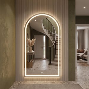Op de afbeelding: Een boogvormige wandspiegel van volledige lengte met een geïntegreerde LED-lichtstrip langs het frame. De spiegel heeft een gladde, gebogen bovenkant en een rechthoekige basis, met twee kleine aanraakgevoelige bedieningspictogrammen onderaan.