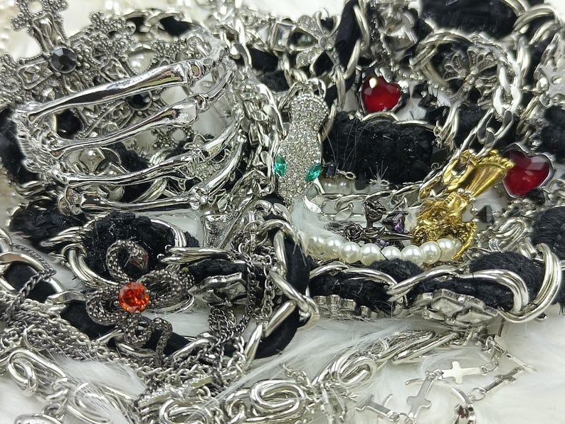 Puede incluir: Un surtido de joyas plateadas, que incluye pulseras, collares y colgantes. La colecci&oacute;n presenta varios dise&ntilde;os, como cruces, corazones y motivos de serpientes. Algunas piezas est&aacute;n adornadas con pedrer&iacute;a y perlas, creando una est&eacute;tica glamurosa y detallada.