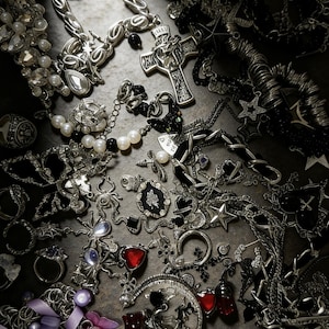 Puede incluir: Una variedad de joyas plateadas, que incluyen collares, anillos y pendientes. La colecci&oacute;n presenta varios dise&ntilde;os, como cruces, estrellas y colgantes en forma de coraz&oacute;n, con acentos de piedras preciosas negras y rojas y perlas.