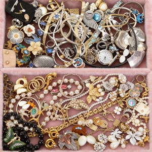 May include: A collection of vintage jewelry, including necklaces, bracelets, rings, and earrings, in gold, silver, and various gemstones. The jewelry is arranged in a pink, plush-lined jewelry box, showcasing a variety of styles and designs.
