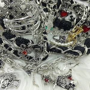Puede incluir: Un surtido de joyas plateadas, que incluyen collares, pulseras y anillos, con detalles en negro y adornos en forma de coraz&oacute;n rojo. La colecci&oacute;n presenta cruces, calaveras y hileras de perlas, creando una est&eacute;tica g&oacute;tica o punk.
