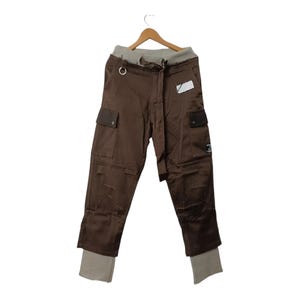 Puede incluir: Pantalón cargo marrón con cintura de cordón y una etiqueta blanca. El pantalón tiene varios bolsillos y un corte holgado.