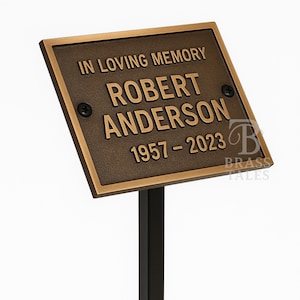 Könnte beinhalten: Bronzene Gedenktafel mit der Inschrift "IN LOVING MEMORY ROBERT ANDERSON 1957-2023". Die Tafel ist auf einem schwarzen Pfahl zur Platzierung in einem Garten oder am Grab befestigt. Die Tafel hat eine rechteckige Form.