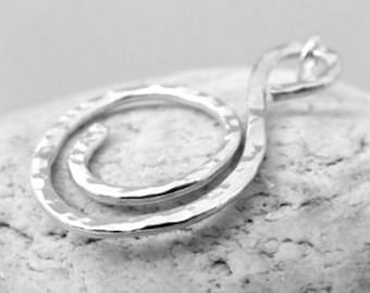 Puede incluir: Collar con colgante de plata con un diseño martillado, retorcido, de doble bucle. El colgante está sobre una roca blanca.