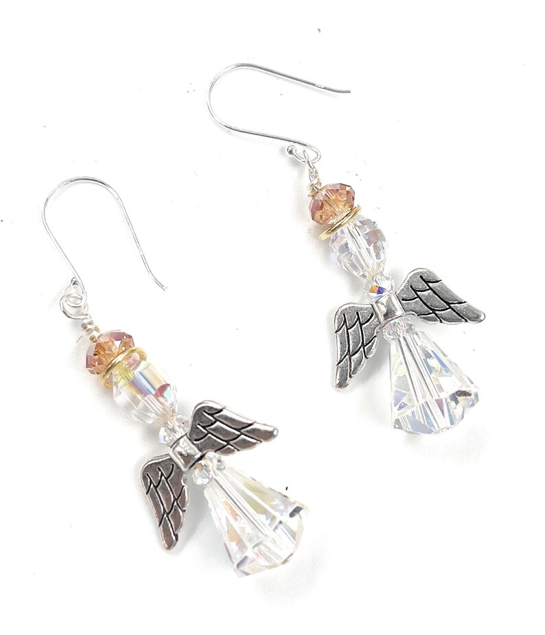 Puede incluir: Un par de pendientes de &aacute;ngel con alas plateadas y cuerpos de cristal transparente facetado. Los pendientes presentan cuentas de cristal iridiscente y ganchos para las orejas plateados. Un accesorio delicado y elegante.