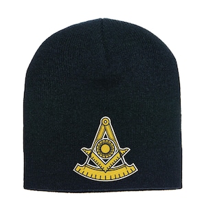 Puede incluir: Un gorro negro con un emblema bordado en amarillo y blanco. El emblema presenta una brújula, una escuadra y un diseño de sol, comúnmente asociado con la masonería. El gorro está hecho de material de punto.