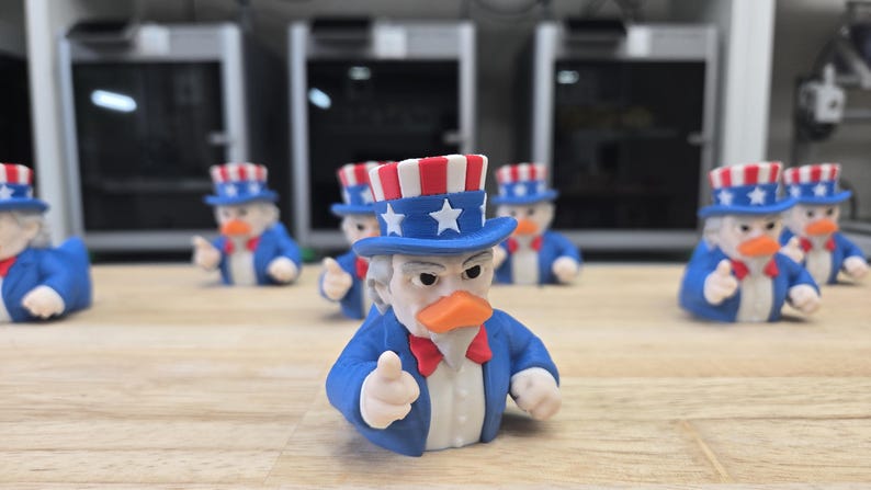 May include: A group of Uncle Sam duck figurines. Each figure is dressed in a blue suit, a red bow tie, and a patriotic hat with red and white stripes and stars. The ducks have orange beaks and are giving a thumbs-up.
