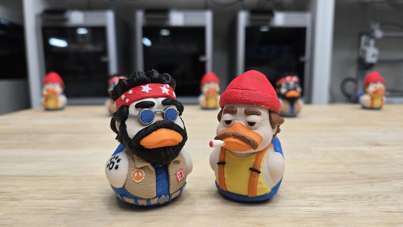 可能包含:两只新奇的橡皮鸭玩具。一只鸭子戴着红色头巾、蓝色眼镜和胡须。另一只鸭子戴着红色小圆帽,叼着香烟。两只鸭子都有橙色的喙,站在木质表面上。背景中还有其他鸭子。