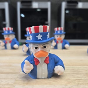 May include: A group of Uncle Sam-themed duck figurines. Each duck is dressed in a blue suit, a red bow tie, and a patriotic top hat with stars and stripes. The ducks are displayed on a wooden surface.