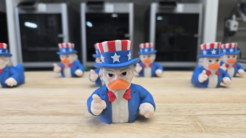 May include: A group of Uncle Sam-themed duck figurines. Each duck is dressed in a blue suit, a red bow tie, and a patriotic top hat with stars and stripes. The ducks are displayed on a wooden surface.