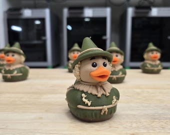 May include: A collection of novelty duck figurines, each dressed as a scarecrow. The ducks have orange beaks, black eyes, and wear green hats and outfits with tan accents. They are arranged on a light-colored wooden surface.