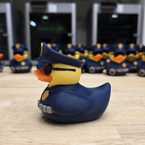 May include: A group of novelty rubber ducks dressed as police officers. The ducks have yellow heads, orange beaks, and wear navy blue uniforms, hats, and sunglasses. They are arranged on a wooden surface.