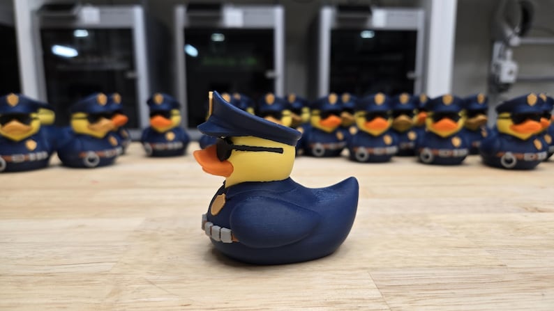 May include: A group of novelty rubber ducks dressed as police officers. The ducks have yellow heads, orange beaks, and wear navy blue uniforms, hats, and sunglasses. They are arranged on a wooden surface.