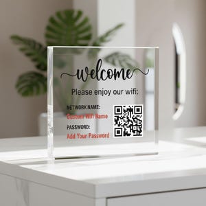 May include: A clear acrylic block with the word "welcome" in cursive script. Below, it reads "Please enjoy our wifi:" followed by network details and a QR code. The text "Custom Wifi Name" and "Add Your Password" are visible.